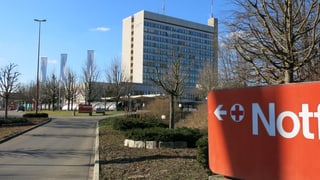 Bruderholzspital von aussen. Am rechten Bildrand sieht man ein grosses, rotes Schild, das den Weg zum Notfall weist.