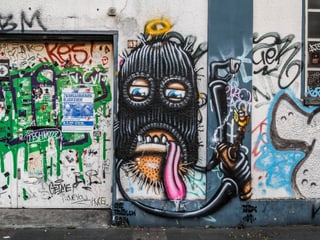 Ein Graffiti mit schwarzer Mütze auf einer Wand.