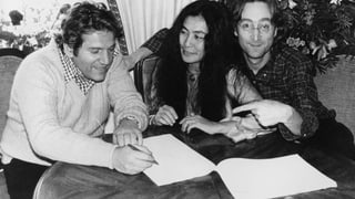 eine schwarz-weiss Aufnahme von John Lennon mit einem Mann, der ein Papier unterschreibt