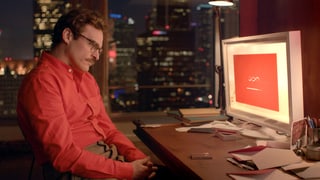 Ein Mann in rotem Hemd sitzt vor einem Computerscreen, der rot aufleuchtet.