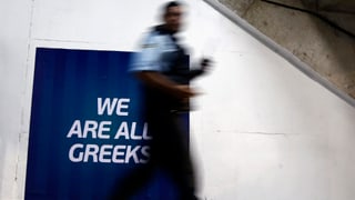 Ein Mann geht an einem Schild vorbei, auf dem steht "we are all greeks", "wir sind alle Griechen".