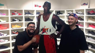 Ein Mann umarmt eine Karton-Version des Basketballspielers Michael Jordan. Im Hintergrund viele Sneaker in Regalen. Ein Mann umarmt eine Karton-Version des Basketballspielers Michael Jordan. Im Hintergrund viele Sneaker in Regalen.