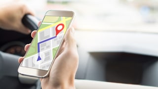 Mann im Auto schaut auf Smartphone mit geöffneter Navigations-App