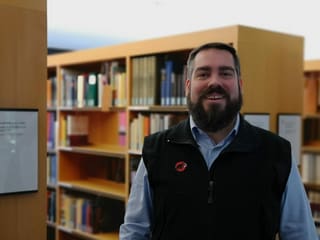 Mann mit Bart vor Bücherregal.