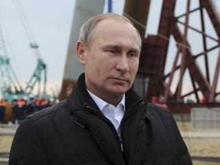 Vladimir Putin steht vor einem Hafenkran, schaut nachdenklich und gedankenverloren aus.