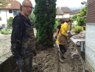 Ein Mann und zwei Frauen stehen in einem Garten voller Schlamm.