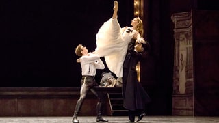 Szene aus der Nussknacker: Zwei Tänzer in Anzug heben eine Tänzerin in weissem Kleid die Luft.