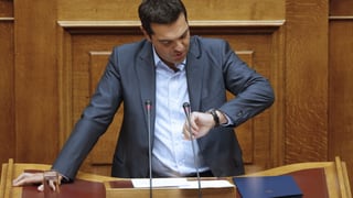 Griechenlands Ministerpräsident Alexis Tsipras schaut am Rednerpult des Parlaments auf seine Uhr.