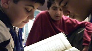 Nahaufnahme: Drei Buben beugen sich über den Koran. 