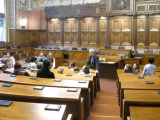 Im Saal des Grossen Rates im Rathaus sitzen Kinder aus demGotthelfschulhaus. Vor ihnen Osi Inglin, der die Bilder an den Wänden erklärt. 