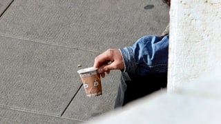 Eine Person (nicht ersichtlich) bettelt mit einem Becher. Eine Person (nicht ersichtlich) bettelt mit einem Becher.