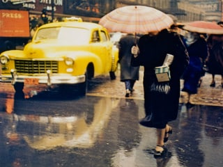 Eine Frau mit einem Schirm über dem Gesicht läuft im Regen vor einem gelben Taxi durch.