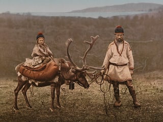 Ein Altes Foto: Ein Mann in traditioneller Kleidung hält ein Rentier, auf dem ein Kind sitzt. Ein Altes Foto: Ein Mann in traditioneller Kleidung hält ein Rentier, auf dem ein Kind sitzt.
