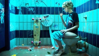 Szenenfoto aus «Feuchtgebiete»: Frau auf Toilette mit Graffiti sitzend