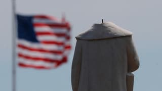 Statue ohne Kopf, im Hintergrund eine wehende US-Flagge.