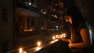 Eine Frau entzündet auf ihrem Balkon Kerzen.