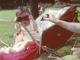 Ein Kleinkind sitzt mit einer übergrossen Sonnenbrille in einem Kinderwagen.