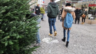 Ein Weihnachtsbaumverkäufer, dahinter Passanten mit Einkaufstaschen.