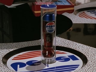Tisch mit runder Unterlage, darauf der Schriftzug «Pepsi». Das Design sieht anders aus als das der richtigen Firma.