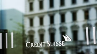 Credit Suisse Schriftzug auf einer Glastüre, in der sich ein Gebäude spiegelt.