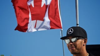 Lewis Hamilton strahlt mit aufgesetzter Sonnenbrille vor der Flagge Kanadas.