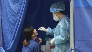 In Schutzkleidung wird eine Frau in einem Zelt aufs Virus getestet.