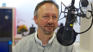 Porträt Thomas Merz vor einem Radiostudio-Mikrofon.