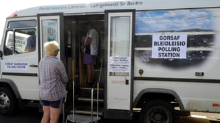 Eine Frau wartet vor einem zum Wahllokal umfunktionierten Bus.
