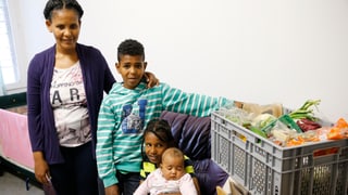 Eine Mutter aus Eritrea mit ihren drei Kindern. Daneben eine Kiste mit Lebensmitteln.
