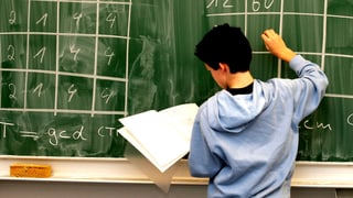 Ein Schüler steht an einer Tafel und schreibt Zahlen in eine Tabelle.