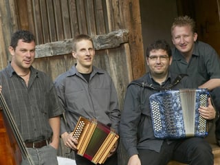 Die vier Musiker mit ihren Instrumenten vor einer Holzscheune.