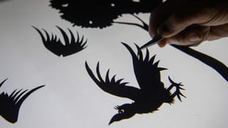 Eine Hand hält einen ausgeschnittenen Vogel mit einer Pinzette fest. Eine Hand hält einen ausgeschnittenen Vogel mit einer Pinzette fest.