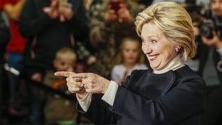 Eine strahlende Hillary Clinton zeigt mit beiden Zeigefingern ins Publikum. 