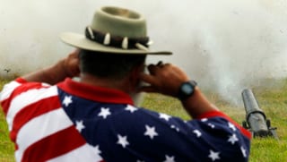 Kanone, dahinter Mann mit T-Shirt, das die US-Flagge zeigt. 