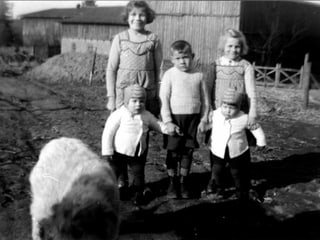 Fünf Kinder stehen auf einem Hof, im Vordergrund ist ein Hund zu erkennen.