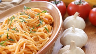 Schüssel mit Spaghetti, daneben hat es Knoblauch und Tomaten schön drapiert.