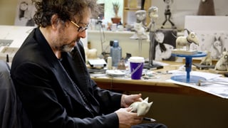 Tim Burton hält eine Figur aus dem Film «Frankenweenie» in den Händen, auf dem Pult stehen weitere Figuren aus dem Film.