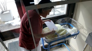Frau steht bei einem leeren Babybett.