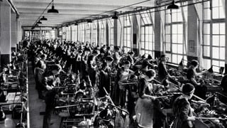 Ein Schwarz-Weiss-Bild: Viele Frauen und Männer arbeiten in einer Revolver-Dreherei. Ein Schwarz-Weiss-Bild: Viele Frauen und Männer arbeiten in einer Revolver-Dreherei.