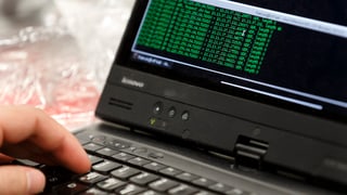 Eine Hand bedient ein Notebook, darauf sind grüne Programmiercodes auf schwarzem Hintergrund zu sehen Eine Hand bedient ein Notebook, darauf sind grüne Programmiercodes auf schwarzem Hintergrund zu sehen