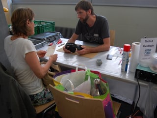 Kundin mit einem Sack voll defekter Elektrogeräte und der Fachmann beraten sich.