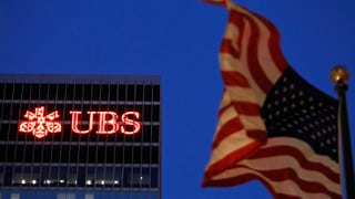 US-Fahne vor einem UBS-Gebäude in New York im Halbdunkeln.