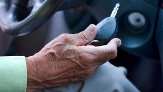 Die Hand einer älteren männlichen Person mit einem Zündschlüssel am Lenkrad.