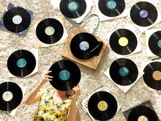 Eine Frau liegt am Boden, auf dem zahlreiche Vinyl-Platten liegen. 