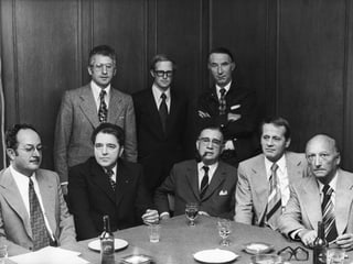 eine schwarz-weiss Fotografie von Männern an einem runden Tisch