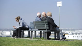 Symbolbild: Auf einer Bank sitzen Rücken an Rücken einige ältere und eine junge Person.