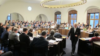 Männer und Frauen sitzen in einem Kreis angeordnet in einem Ratssaal.