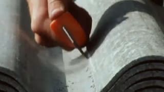 Ein Mann ritzt mit einer Klinge eine Eternit-Platte, wobei Staub aufwirbelt.