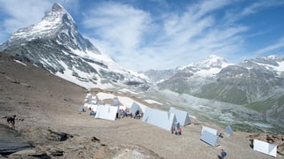 Zelte aus Holz und Aluminium stehen auf dem steinigen Boden, dahinter das Matterhorn