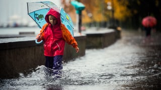Ein Kind mit Schirm und wasserfesten Hosen, stapft durch das überflutete Ufer des Lago Maggiores